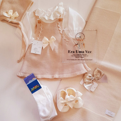 Conjunto de roupa de bebé em tons creme com vestido de malha e outros acessórios