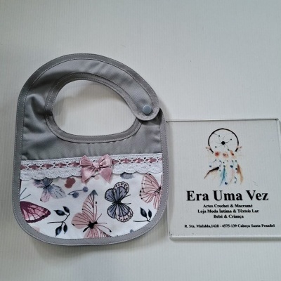 Babete para bebé cinzento com padrão de borboletas, laço rosa e renda branca.