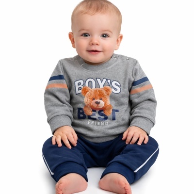 Bebé com camisola cinzenta com urso e calças azuis sentado em fundo branco