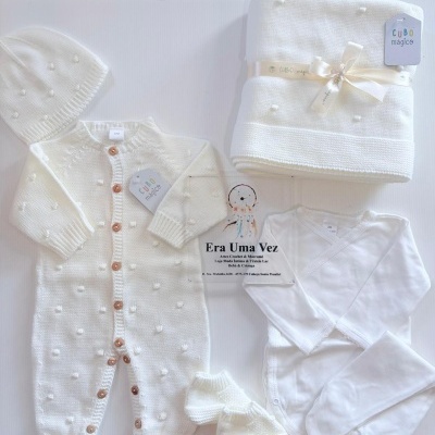 Conjunto de roupa de bebé branco com padrões de bolinhas em relevo e manta dobrada.