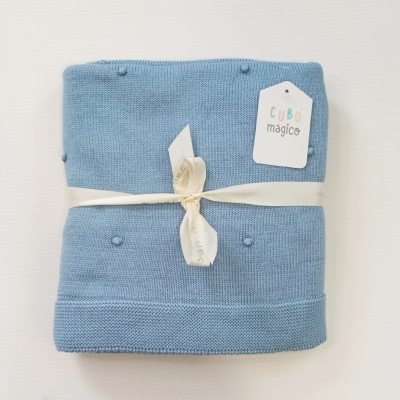Manta de malha azul claro dobrada com etiqueta CUBO mágico