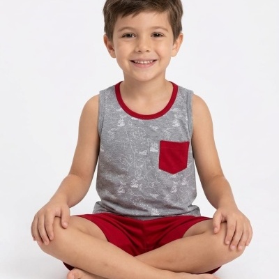 Menino a sorrir vestido com camisola cinza com bolso vermelho e calções vermelhos sentado.