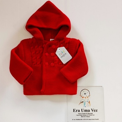 Casaco de malha vermelho com etiqueta sobre superfície branca e placa com texto ao lado.