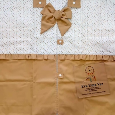 Produto têxtil branco com estrelas castanhas e tecido castanho com laço e botões com estrelas brancas.