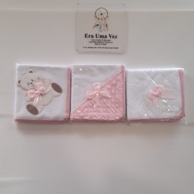 Três panos de bebé brancos com detalhes rosa, embalados individualmente em plástico.