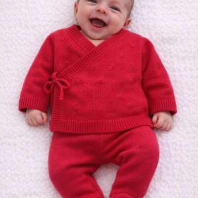 Bebé a sorrir com conjunto de malha vermelha e calças com pés