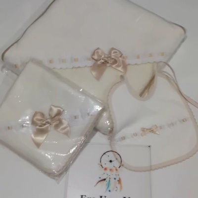 Conjunto de tecido para bebé branco com laços em cetim bege e embalagem transparente.