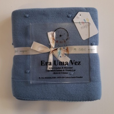 Cobertor azul de malha com pompons, fita branca e etiquetas com texto