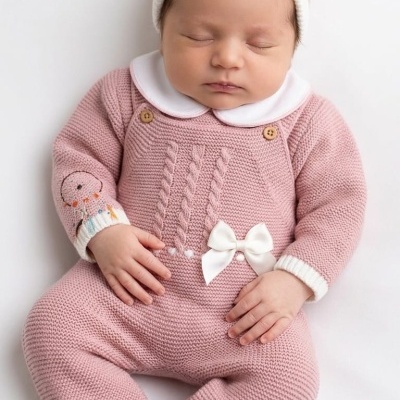 Bebé a dormir com macacão e gorro rosa em malha com laço branco.
