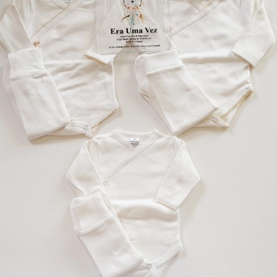 Três conjuntos de roupa de bebé branca com body de manga comprida e calças, placa acrílica com texto em português.