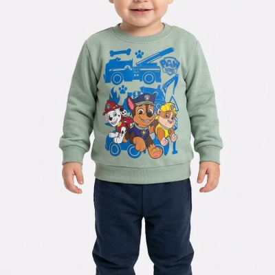 Criança com camisola verde Paw Patrol e calças azuis escuras em fundo branco