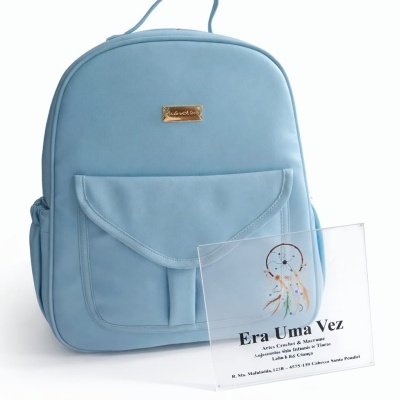 Mochila azul clara com bolso frontal e placa metálica