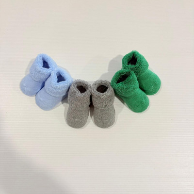 Três pares de meias felpudas para bebés azul, cinzento e verde em superfície branca.