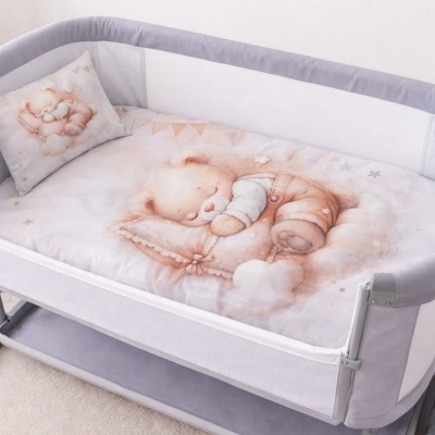 Berço de bebé cinzento com colchão e almofada com desenho de urso a dormir.