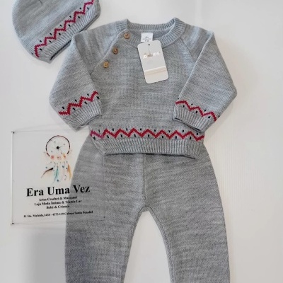 Conjunto de bebé cinza em malha com padrão vermelho e preto e botões de madeira, colocado sobre fundo branco com placa de loja