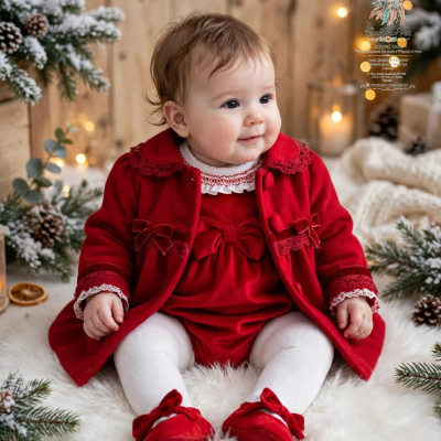 Bebé vestida de vermelho com laços e renda sentada num tapete branco com decoração natalícia ao fundo.