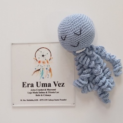 Brinquedo de croché azul claro com forma de polvo ao lado de placa com informações da loja
