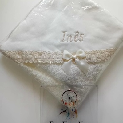 Toalha branca bordada com nome Inês, laço, embalagem plástica e placa com texto Era Uma Vez