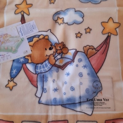 Manta infantil com desenho de urso a ler, estrelas e luas amarelas e azuis.