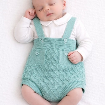 Bebé a dormir com body branco e calções verdes de malha com alças e botões