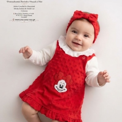 Bebé com vestido vermelho e banda de cabelo com laço vermelho.