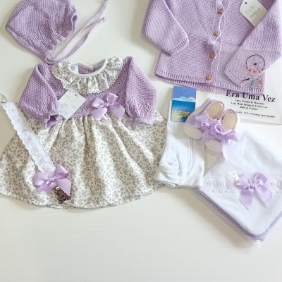 Conjunto de roupa de bebé lilás e branco com vestido, casaco, capuz, sapatinhos e acessórios.