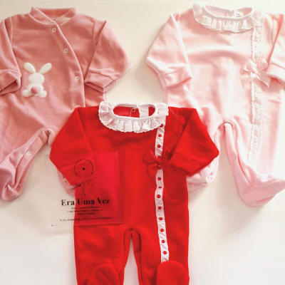 Três pijamas de bebé rosa e vermelho com rendas e laços sobre superfície branca