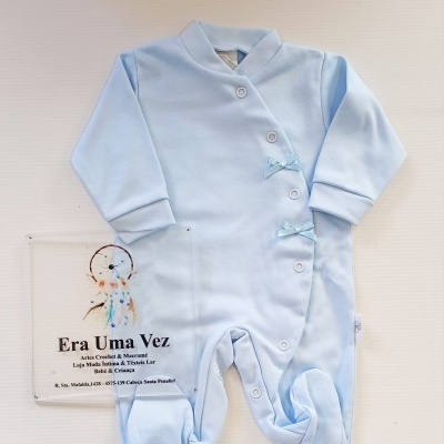 Pijama azul claro para bebé com botões e laços decorativos colocado sobre fundo branco