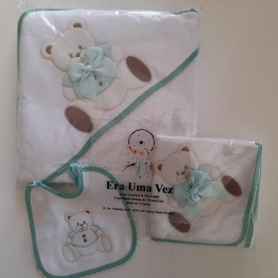 Conjunto de têxteis para bebé branco e verde com ursinhos bordados e laços azuis, embalados em plástico.