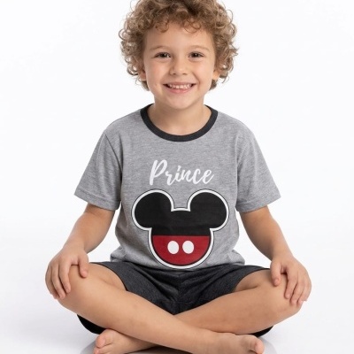 Criança sentada de pernas cruzadas a usar t-shirt cinzenta com estampa Prince e personagem de rato preto e vermelho.