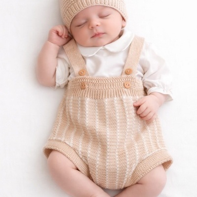 Bebé com roupa de malha creme e body branco, deitado