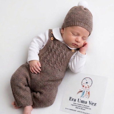 Bebé com fato e gorro de malha castanha e cartão branco com texto e desenho ao lado.