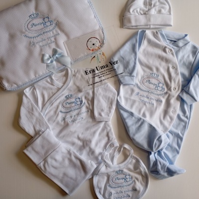 Conjunto de roupa de bebé azul e branca com bordados de coroa e ursinho, com texto 'Príncipe A minha primeira roupinha'