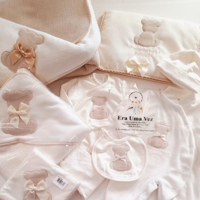 Conjunto de roupa e acessórios para bebé com ursinhos bordados e laços em branco e bege.