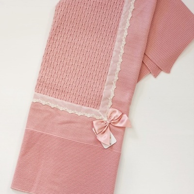 Manta rosa com padrões tricotados, renda branca e laço de cetim em fundo branco