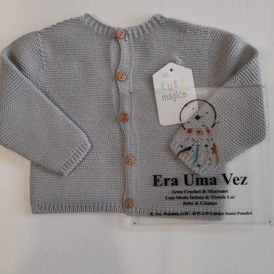 Casaco de malha cinzento claro para bebé com botões de madeira e etiquetas, sobre folha transparente com texto impresso.