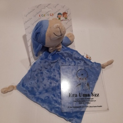 Peluche azul com cabeça bege e gorro, embalagem e etiqueta com texto