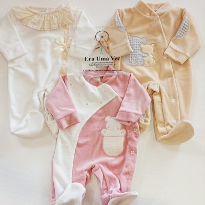Três macacões de bebê em tecido felpudo de cores branca, rosa e bege, com detalhes bordados e gola folhada