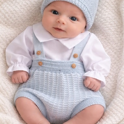 Bebé vestido com roupa de malha azul claro e camisa branca deitado em tecido branco