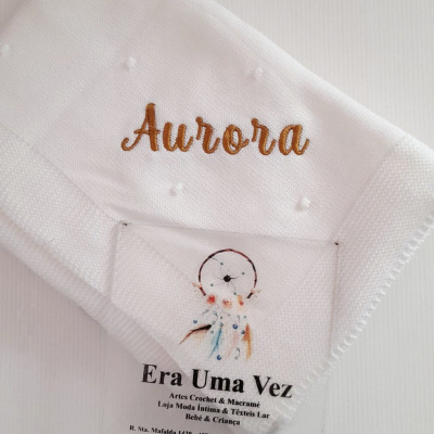 Fralda branca bordada com o nome Aurora e cartão de loja