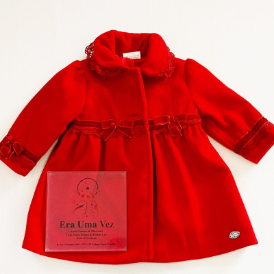 Casaco vermelho para criança com renda e laços decorativos, disposto sobre fundo branco com cartão vermelho ao lado.