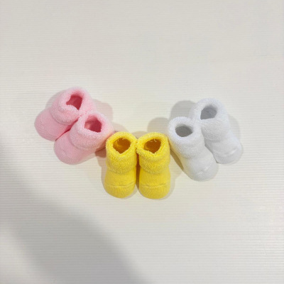 Três pares de botins de bebé em rosa, amarelo e branco sobre fundo claro.