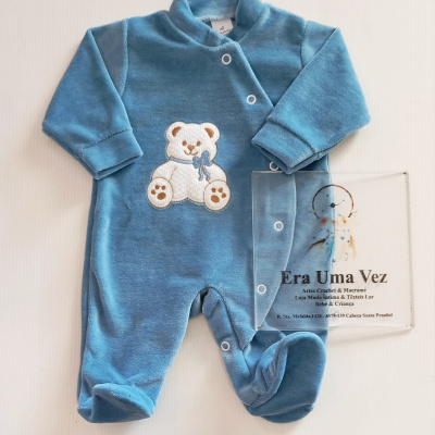 Pijama azul de bebé com ursinho bordado e placa transparente com texto sobre loja.