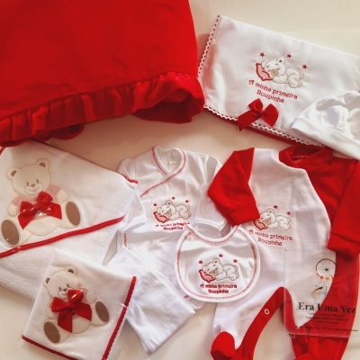 Conjunto de roupa para bebé branco e vermelho com bordados de ursos e texto A minha primeira Roupinha, e manta vermelha com folhos.