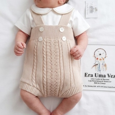 Bebé com roupa de malha bege e body branco deitado