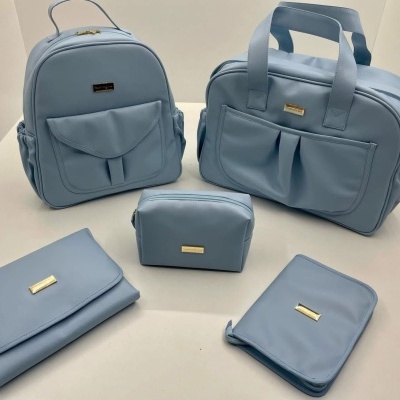 Conjunto de cinco bolsas em pele azul clara com etiquetas douradas, sobre uma superfície branca