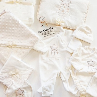 Conjunto creme para bebé com bordados de estrela e texto, inclui body, babete, toalhas, touca e fita de chupeta.