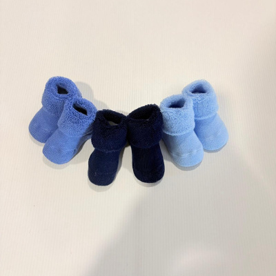 Três pares de meias de bebé em azul médio, azul escuro e azul claro dobradas sobre fundo branco.