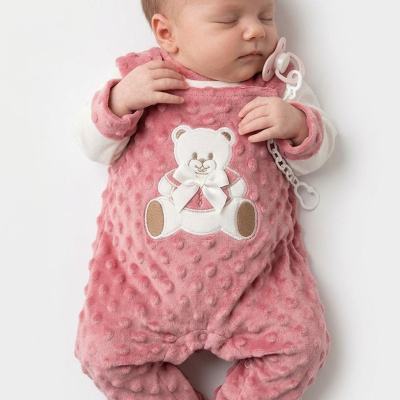 Bebé a dormir com roupa rosa texturada e peluche de ursinho, a segurar chupeta com clip.