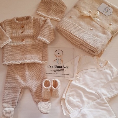 Roupa e acessórios de bebé em tons bege e branco com manta e etiqueta